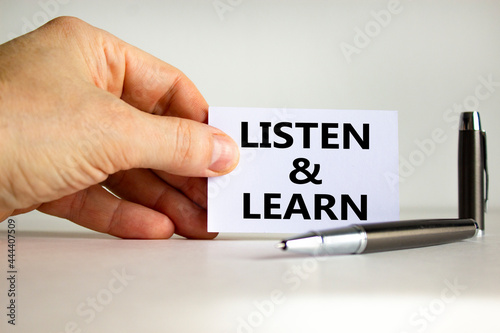 Listen and learn symbol. White paper with words 'Listen and learn' in businessman hand, metallic pen. Beautiful white background. Business, educational and listen and learn concept. Copy space.
