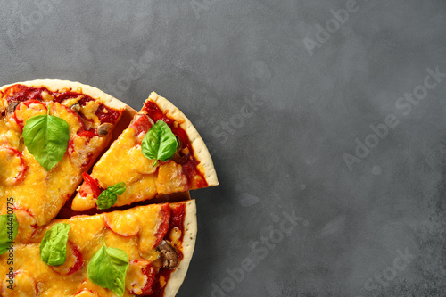 Top view of hot tasty homemade pizza with green basil leaves on the dark grey concrete background. Italian pizza on the black slate tabletop. With copy space for text. Flat lay, close-up