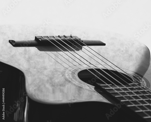 A close up of a classical acoustic guitar with an Different parts of a guitar such as strings, neck, frets, case, bridge. Black and white photography