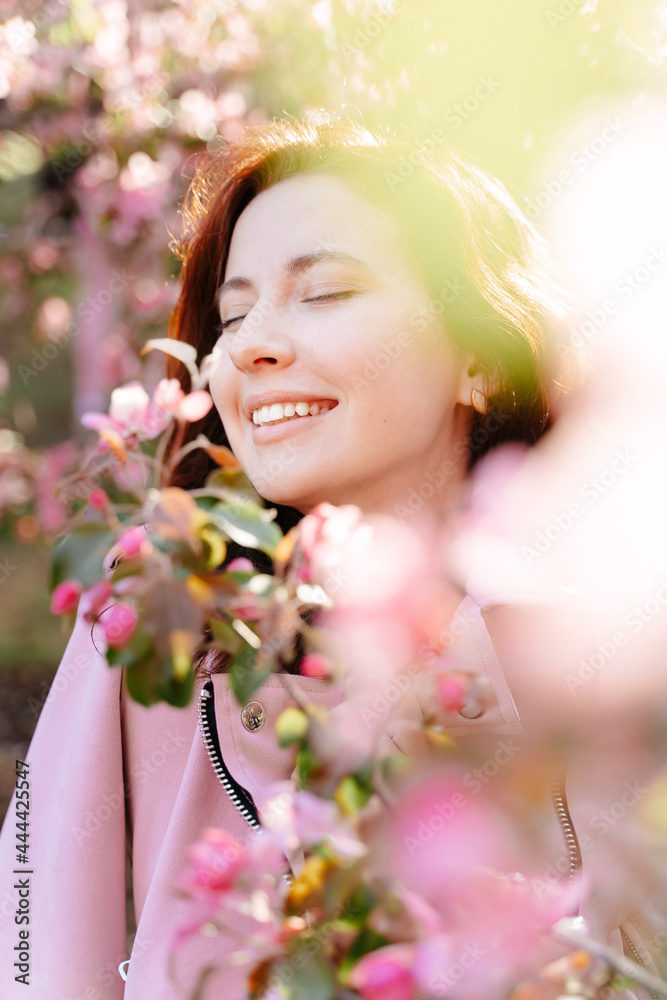 Close-up portrait of a young girl with a smile on her face standing around a blooming rose tree in the garden. The concept of spring and allergy to blossom. Close-up portrait of a young girl with a smile on her face standing around a blooming rose tree in the garden. The concept of spring and allergy to blossom.