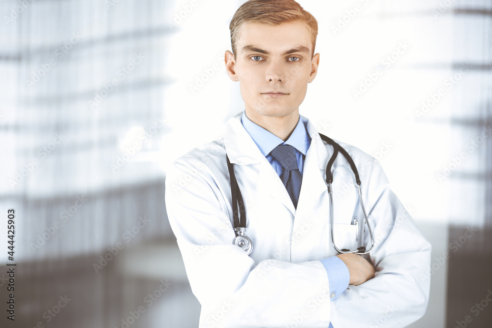 Doctor man, with a stethoscope, stands at his sunny hospital office. Perfect medical service in clinic. Happy future in medicine and healthcare Doctor man, with a stethoscope, stands at his sunny hospital office. Perfect medical service in clinic. Happy future in medicine and healthcare
