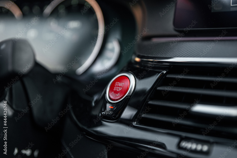 Sports car dashboard with focus on red engine start stop button. Button engine start and engine stop. Car inside. Ignition remote starter. Modern car interior details. Selective focus.