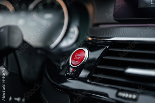 Sports car dashboard with focus on red engine start stop button. Button engine start and engine stop. Car inside. Ignition remote starter. Modern car interior details. Selective focus.