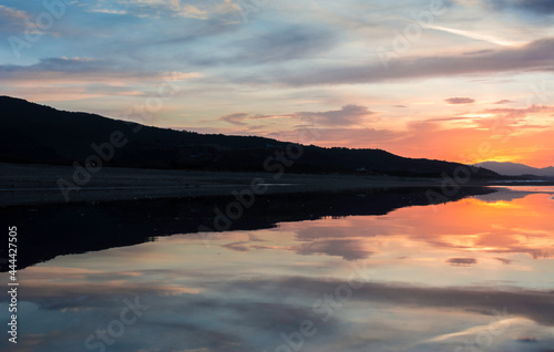 Reflection of mountains on the Mediterranean beach with sunset, clouds and sky, seascape of the Mediterranean coast, sandy coastal strip, reflection in a pool of water.