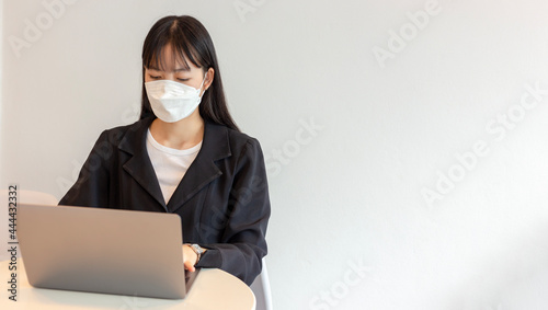 Young asian woman wear white mask and using laptop in white background. Beautiful asian woman wear white mask and working from home. selective focus on a woman.