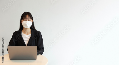 Young asian woman wear white mask and using laptop in white background. Beautiful asian woman wear white mask and working from home. selective focus on a woman.