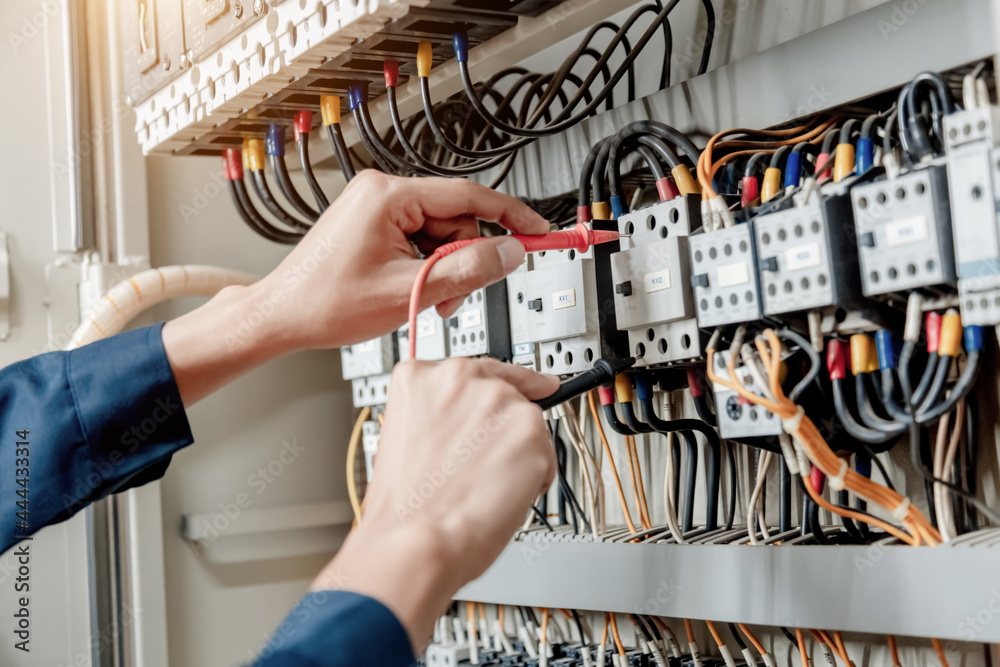 Electrician engineer uses a multimeter to test the electrical installation and power line current in an electrical system control cabinet. Electrician engineer uses a multimeter to test the electrical installation and power line current in an electrical system control cabinet.