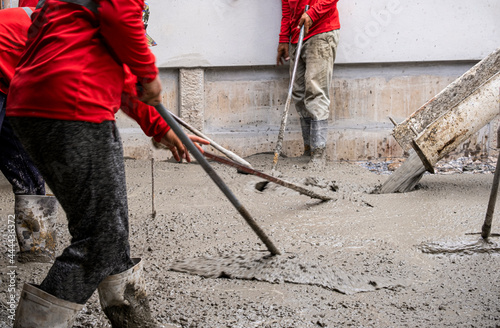three worker team working wet cement on floor by use trowel with long Tools spreading poured concrete for strong street after dry.