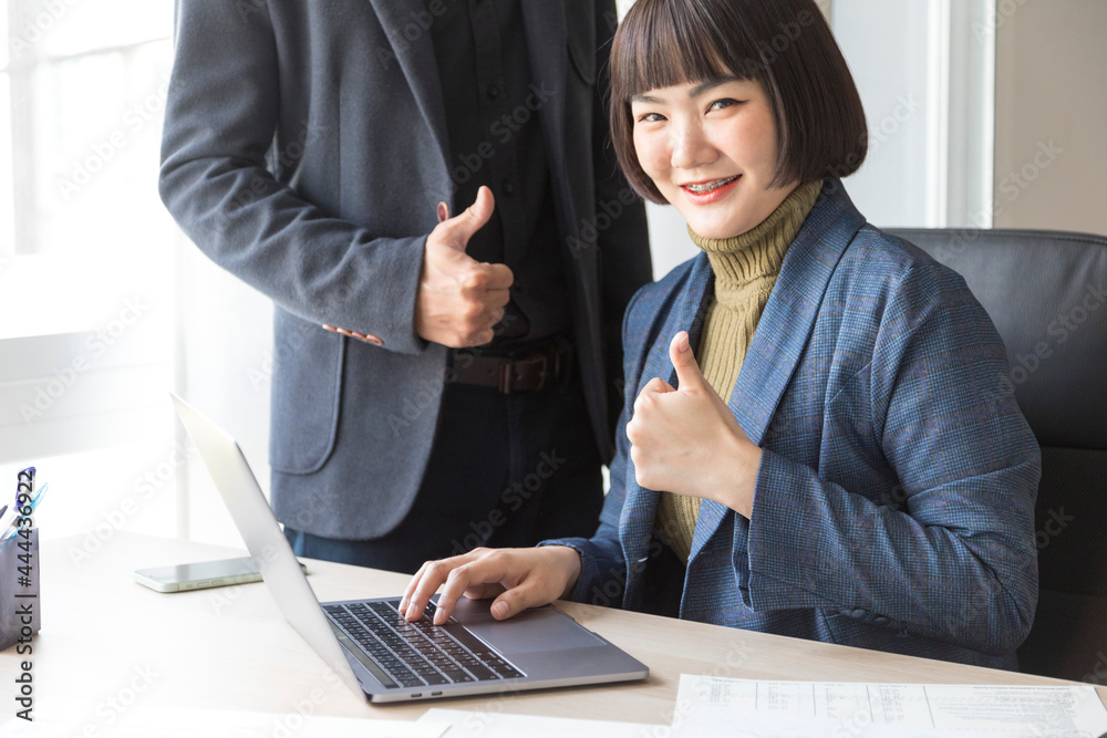 Happy of businesswoman and businessman showing thumbs up sign with computer on wooden table in office background. Happy of businesswoman and businessman showing thumbs up sign with computer on wooden table in office background.