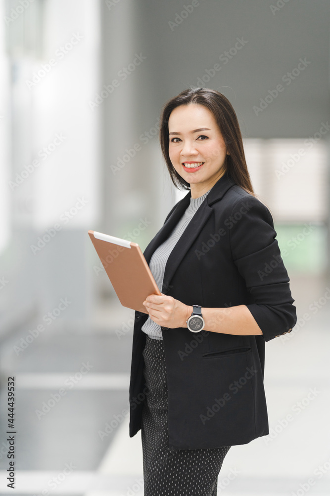 Portrait of a cheerful confident Asian businesswoman in a business suit standing whie using a digital tablet in the business building. Business stock photo Portrait of a cheerful confident Asian businesswoman in a business suit standing whie using a digital tablet in the business building. Business stock photo
