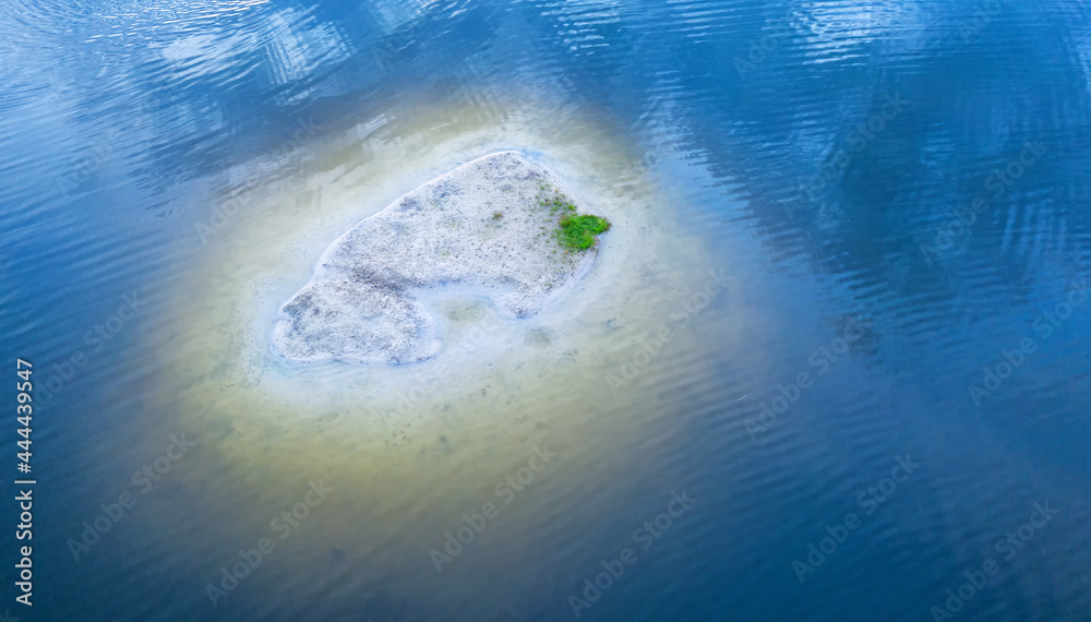 Fototapeta premium A small sandy island surrounded by blue water.