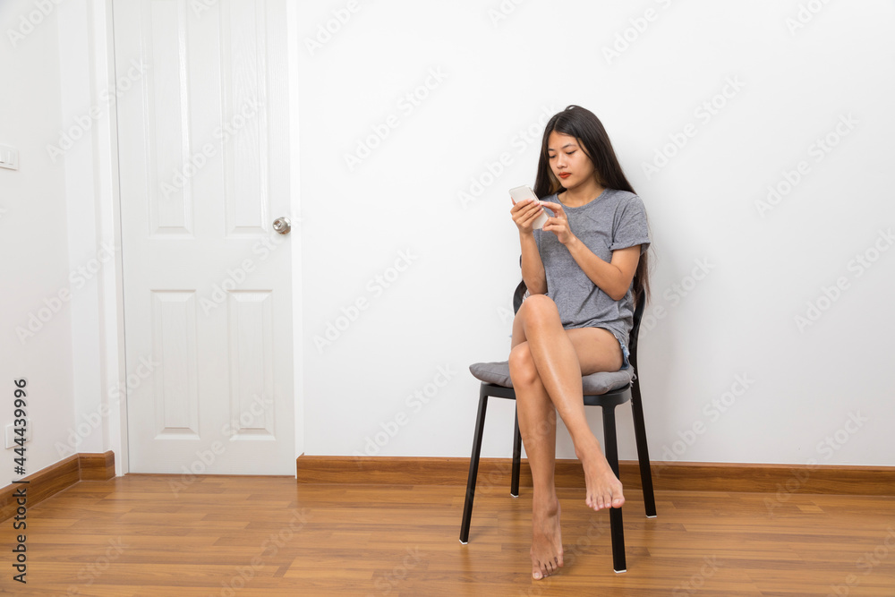 Beautiful young Asian woman smiling sitting relax in the room, using smart phone on white background.