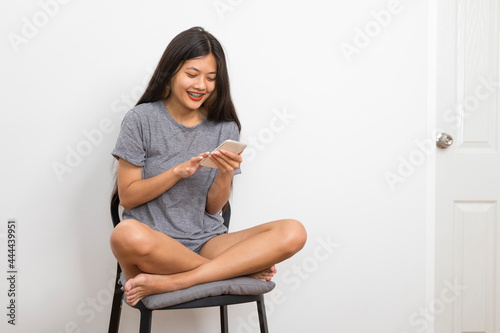 Beautiful young Asian woman smiling sitting relax in the room, using smart phone on white background.