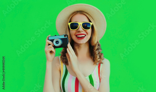 Summer portrait of happy smiling young woman with retro camera wearing a straw hat on green background