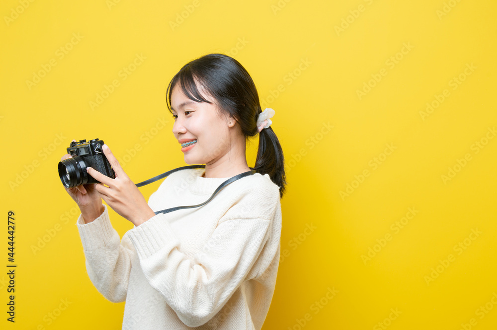 Portrait of a surprise girl with a camera in hand on a yellow background. Isolated studio.