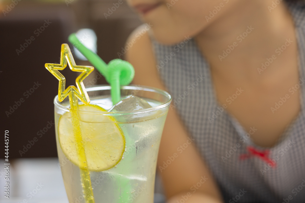 Φωτογραφία Close up and selective focus shot of lemonade soda in cocktail glass with fancy straw and lemon slice decoration in blurred background of adorable kid girl drinking for her refreshment