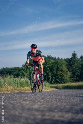 Vertical Angled photo, of a young woman professional cyclist, riding speed her road bike, on a paved road amidst nature, illuminated by sunlight. Sport Equality concept.