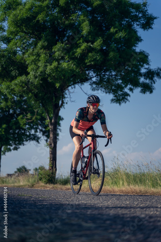 Vertical, Angle photo of a young woman, pedaling, riding speed a road bike, on a ride through nature. Gender equality in sport Concept.