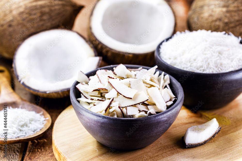 coconut chips, shavings and pieces of coconut inside a clay bowl, with many ripe coconuts in the background