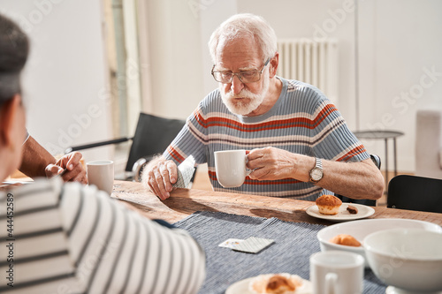 Senior man holding cup of tea and playing at the cards