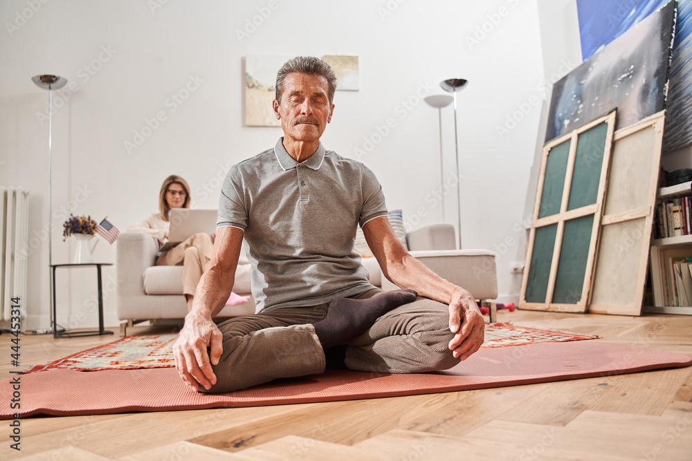 Man in casual clothes meditating and sitting at lotus pose with closed eyes