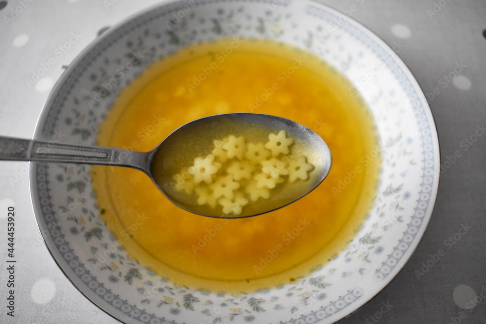 Hot bowl of chicken soup and spoon with soup and flowers noodles Hot bowl of chicken soup and spoon with soup and flowers noodles