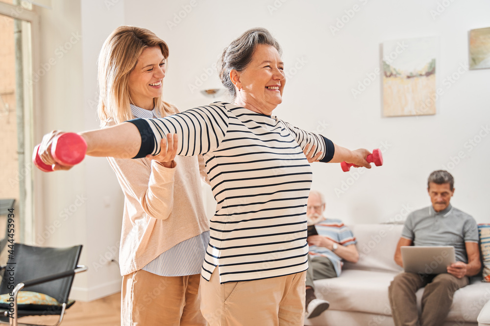 Woman training with dumbbells with her caregiver at the nurse house