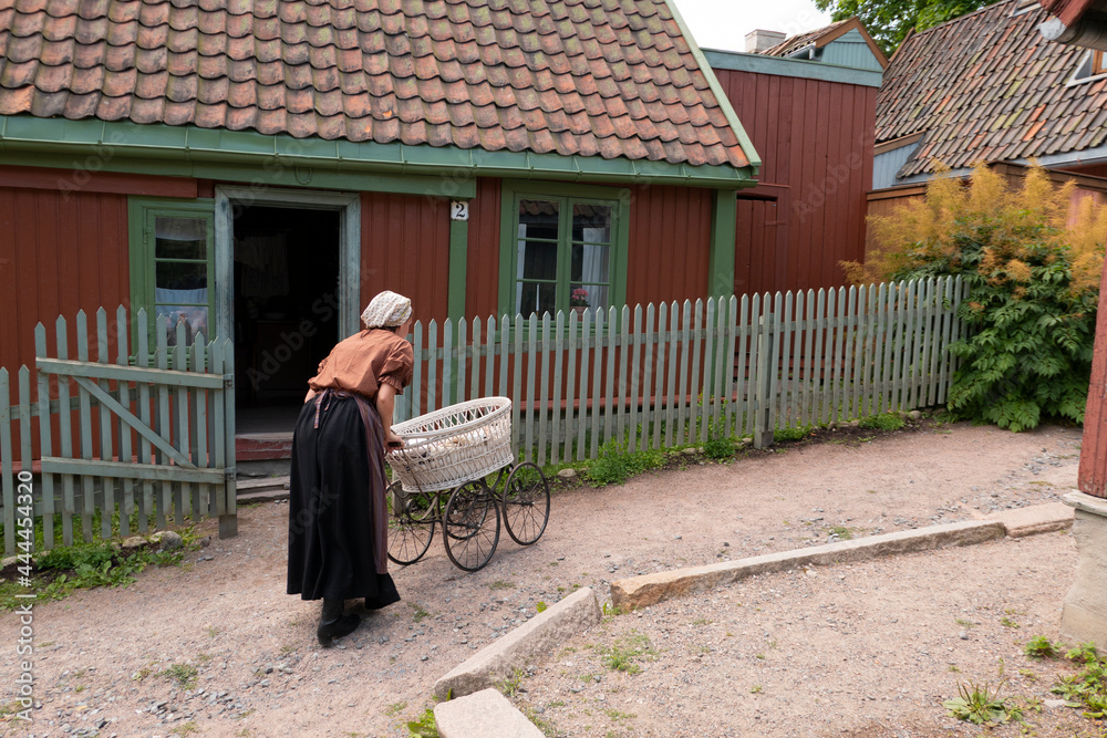 female in old clothes with vintage stroller old exterier in village
