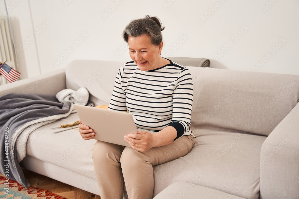 Senior woman holding laptop at her knees and smiling while chatting with relatives Senior woman holding laptop at her knees and smiling while chatting with relatives