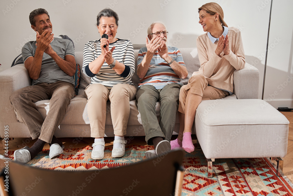 Group of senior people singing while sitting at the sofa with their caregiver