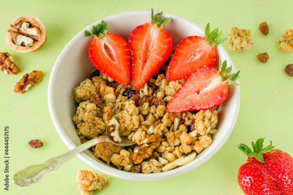 Healthy breakfast in a white bowl with natural granola. Homemade baked muesli, nuts, fresh strawberries on a green background. Healthy breakfast in a white bowl with natural granola. Homemade baked muesli, nuts, fresh strawberries on a green background.