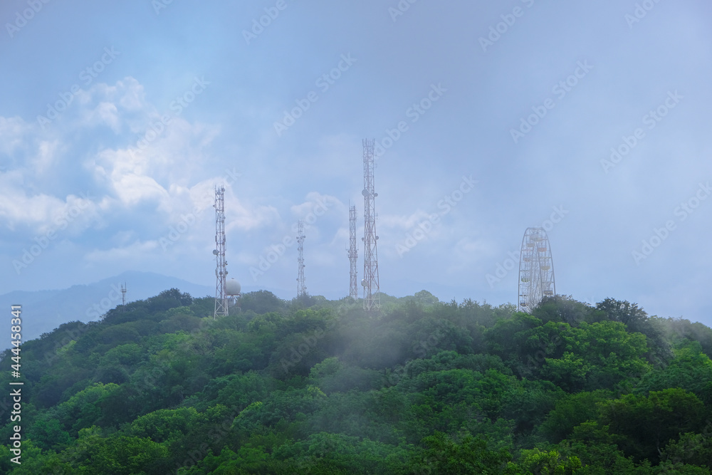 Obraz premium View of mountains and forest in the fog mist, landscape of mountain Akhun hills with radio towers and a Ferris wheel in the morning haze with noise film grain effect, soft selective focus