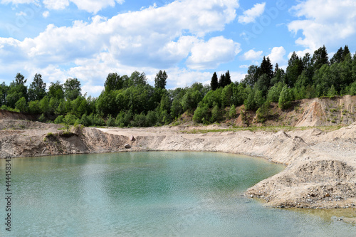 Flooded quarry with blue water. Sandy hills, blue sky, water and trees. Summer sunny landscape. Beautiful nature. Lake in the park.