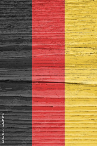 The flag of Germany on dry cracked wooden surface. It seems to flutter in the wind. Vertical background or backdrop with German national symbol. Hard sunlight with shadows on old wood