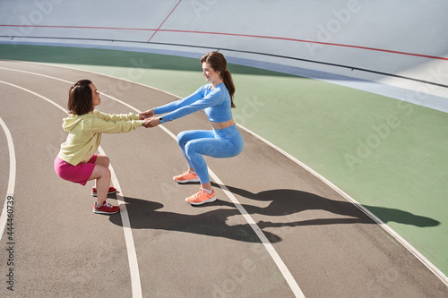 Two girls doing squats at the track at the stadium together