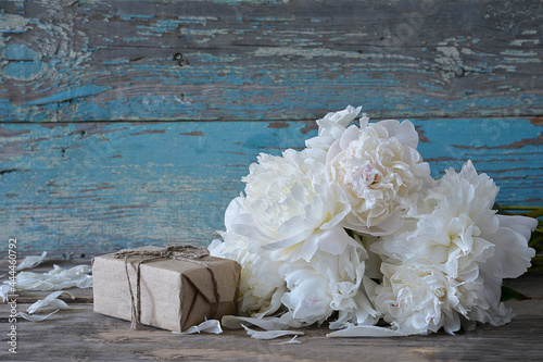 Bunch of white peonies and hand made gift box on old paint wooden background photo