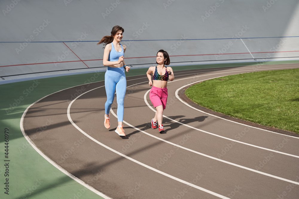 Fototapeta premium Woman running during sunny morning on stadium track with her midget friend