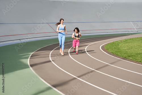 Woman running during sunny morning on stadium track with her midget friend