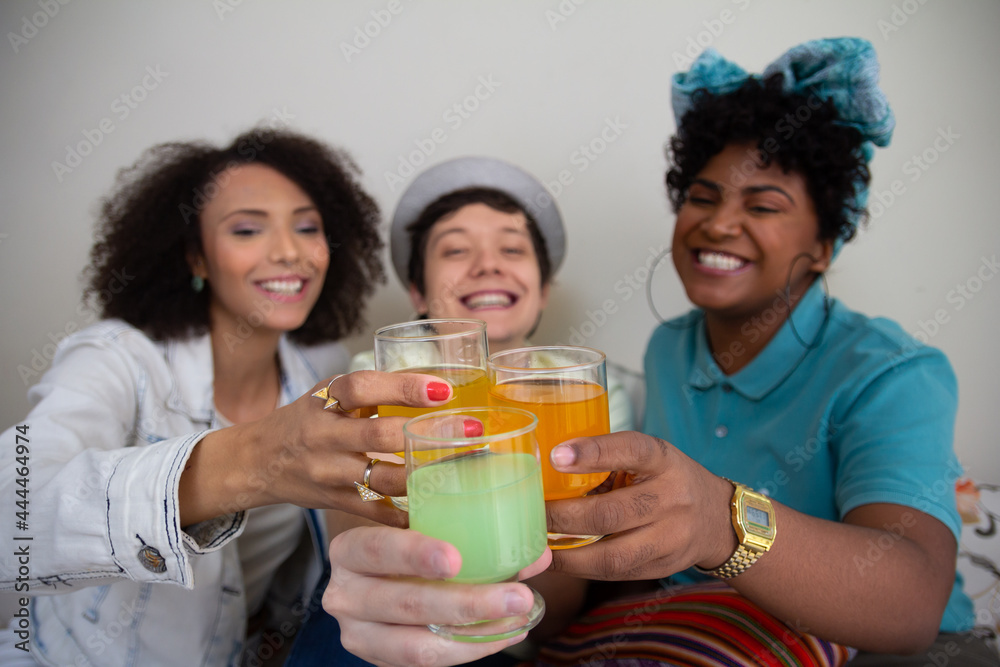 Three multi ethnic friends with colorful cups attached for a toast in the foreground sitting in living room. Time of fun, bonding and good vibes Three multi ethnic friends with colorful cups attached for a toast in the foreground sitting in living room. Time of fun, bonding and good vibes
