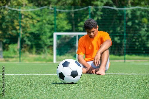 Soccer ball close up against soccer goal and loser sitting on sports field