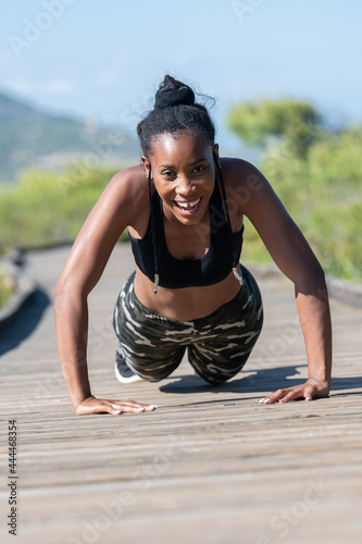 Struggling afro american woman doing push ups on a wooden runway: Exercise and effort concept.