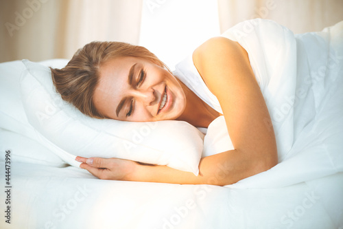 Beautiful blonde girl sleeping sweetly in sunny bedroom on a white bed. Holyday comfort and Rest concepts