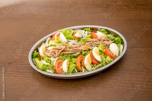 Metal salad tray to share with lots of iceberg lettuce, tomato and chopped boiled egg, slices of white onion and canned tuna on top.