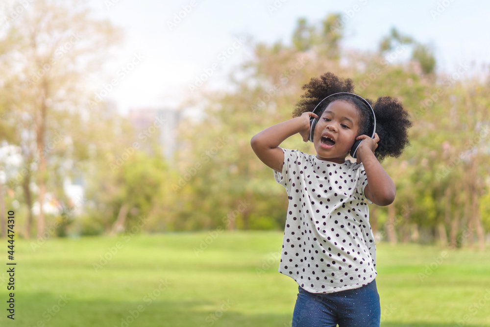 Happy african little girl have big smile, her listening music with headphones and dancing at outdoors park. Happy african little girl have big smile, her listening music with headphones and dancing at outdoors park.