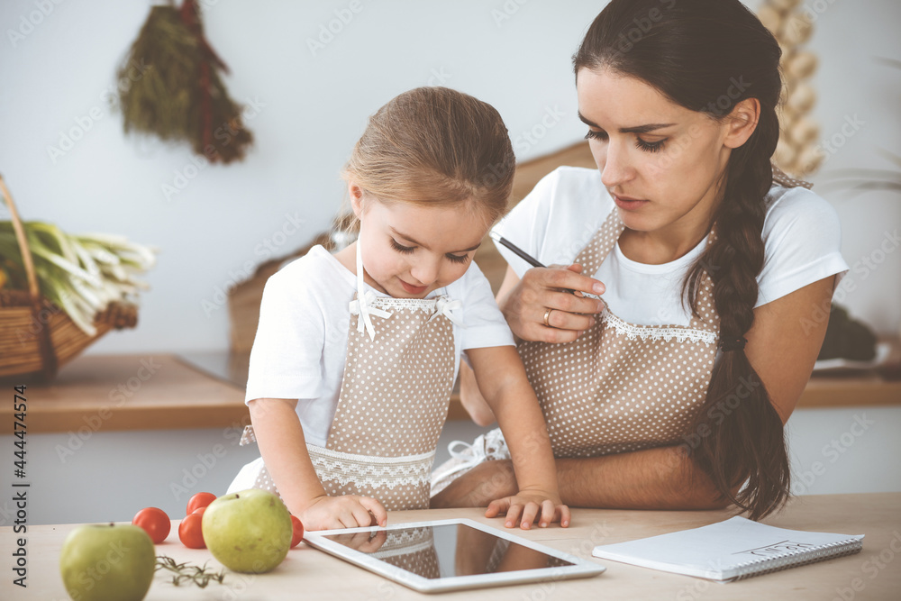 Happy woman and her daughter are searching for new recipes for a delicious family feasting. Christmas, New year, Thanksgiving, Anniversary, Mothers Day. Healthy meal cooking concept Happy woman and her daughter are searching for new recipes for a delicious family feasting. Christmas, New year, Thanksgiving, Anniversary, Mothers Day. Healthy meal cooking concept