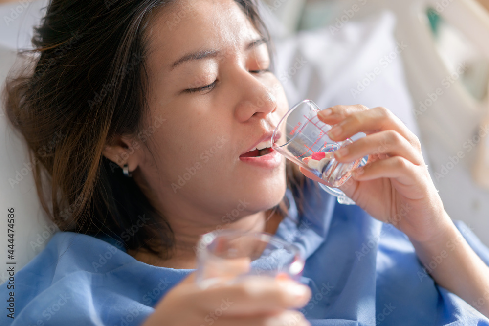 Asian woman patient with medical drip or IV drip drinking water with medicine in hospital ward, Selective focus, Healthcare concept. Asian woman patient with medical drip or IV drip drinking water with medicine in hospital ward, Selective focus, Healthcare concept.