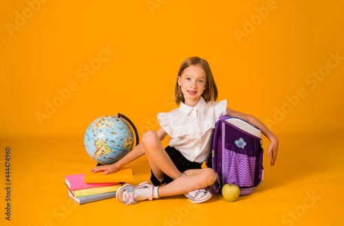 happy schoolgirl in uniforms is sitting with school supplies and a globe on a yellow background with a copy of the space photo