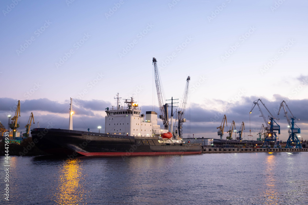 Sea ship in  cargo port. Cargo ship in port. Loading cranes in background. Transportation of cargo by sea. Ship is waiting for loading of containers in port. Concept - sea logistics.