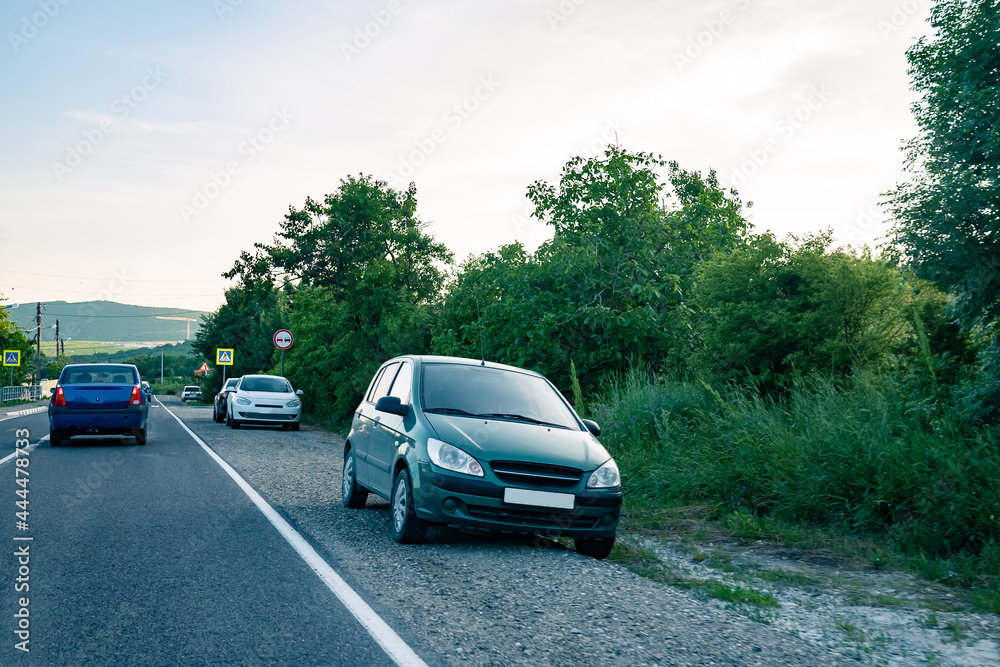 Fototapeta premium Parked cars on the sidelines on a country road. Cars on the edge of a road in the countryside during the day.