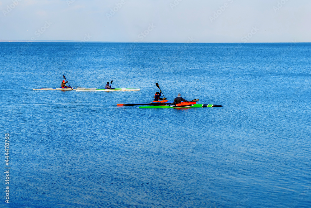 A company of young people on kayaks is training at sea. Four multi-colored canoes sail in the blue sea. Spring canoe training on the high seas.